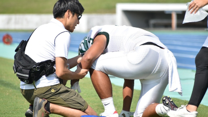 トレーナーがグラウンドで選手の腕をサポートしている様子